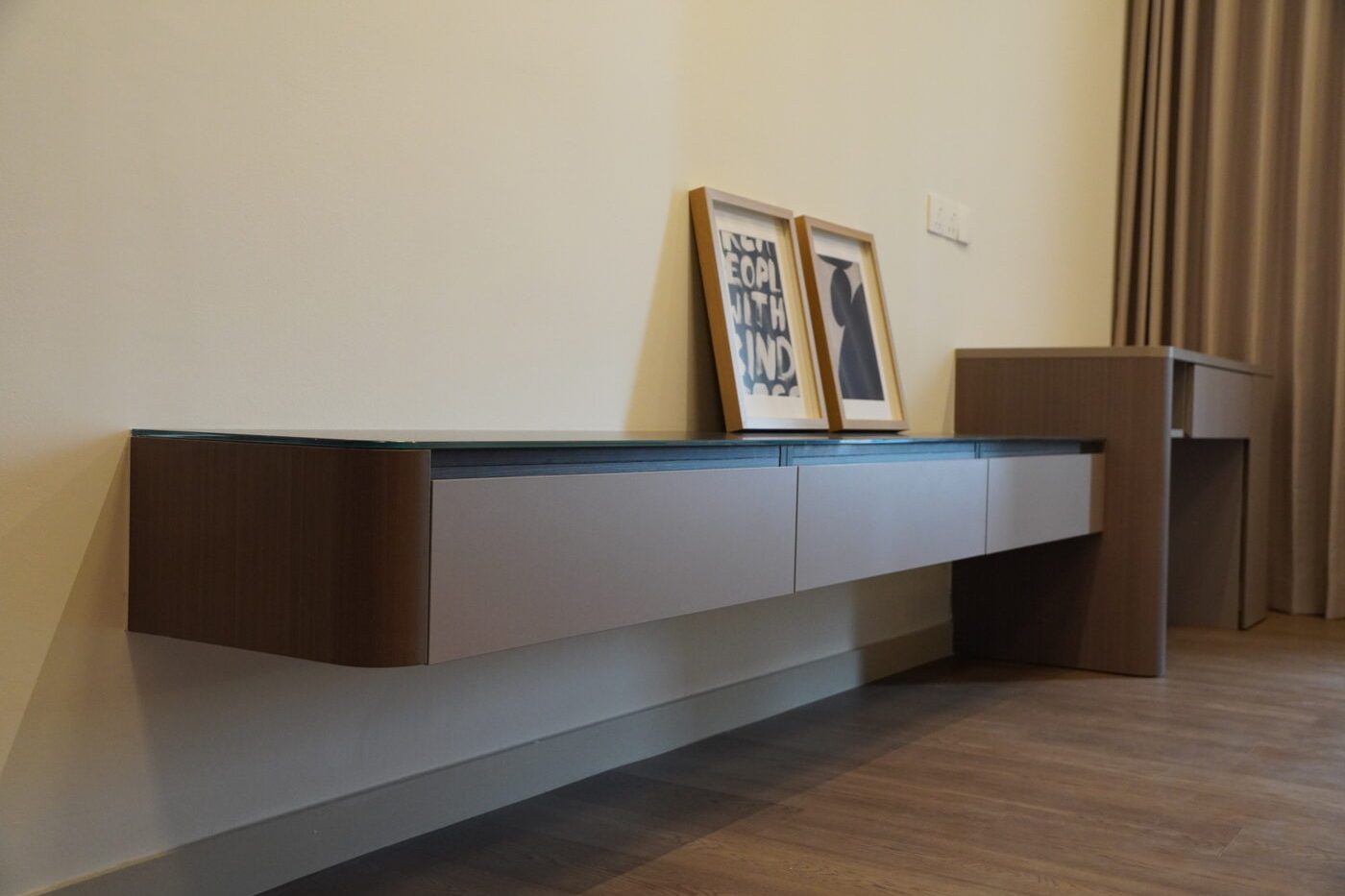Floating console with a rounded timber-veneer end and matte grey-beige drawer fronts