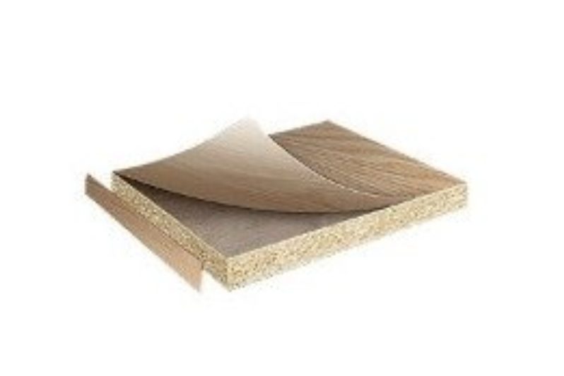 Board sample with wood-grain laminate peeled back from a particleboard core, showing the cut edge