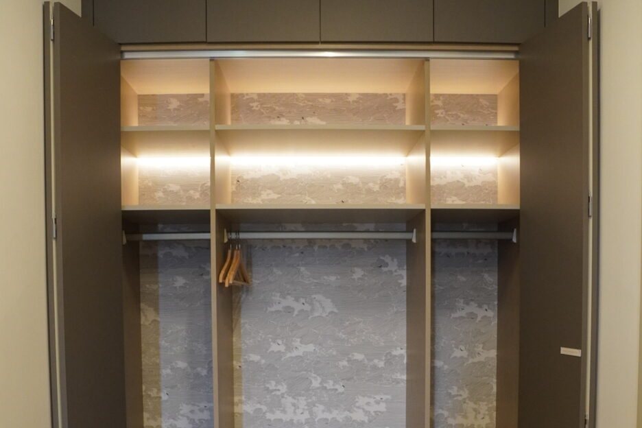 Open built-in wardrobe with lit shelves and hanging rails